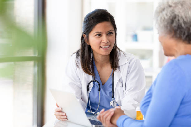 Female patient listens carefully to mid adult female doctor The unrecognizable senior patient listens carefully to the mid adult female doctor.  The doctor is explaining something on the laptop. doctor patient stock pictures, royalty-free photos & images