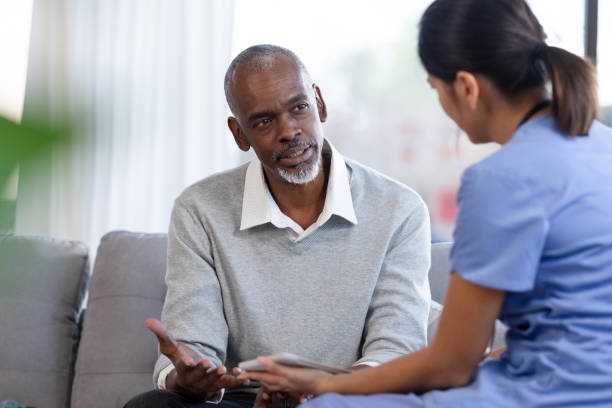 istock Senior man gestures while speaking with nurse in his home 1224859673