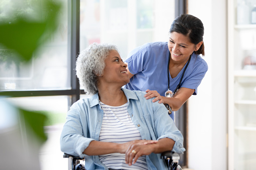 A mid adult female doctor pauses to encourage the senior woman sitting in a wheelchair.
