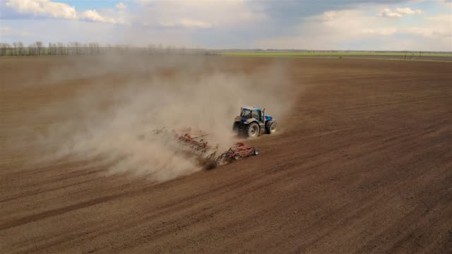Aerial footage of modern blue tractor with red plough plowing or cultivating large field