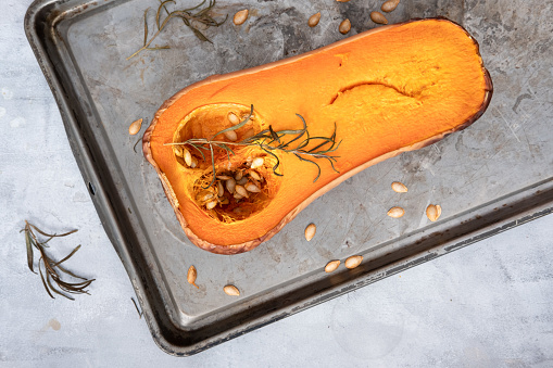 Half a butternut roasted on a baking tray with rosemary on a grey background