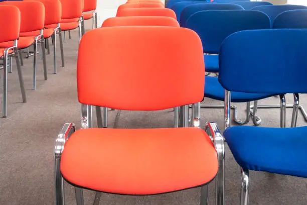 Chairs red and blue in row. Empty seats in a meeting room or auditorium. Selective focus. No people.