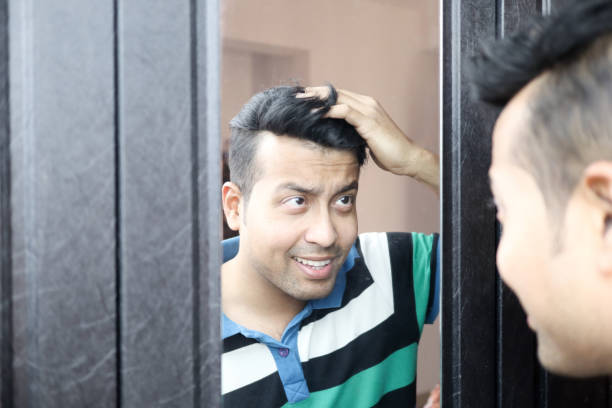 un indio en camiseta casual hombre mirando su reflejo en el espejo y el peinado del pelo. - male towel men human face fotografías e imágenes de stock