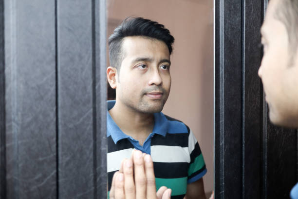 istock a man in casual t-shirt looking at his reflection with vacant expression. 1224870248
