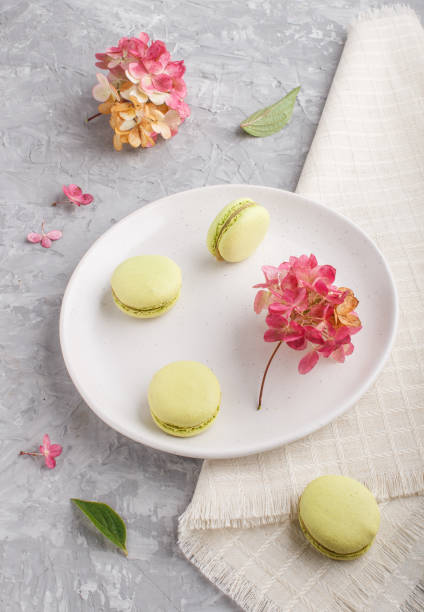 istock Green macarons or macaroons cakes on white ceramic plate on a gray concrete background and linen textile. side view, close up. 1224870275