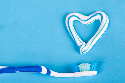 Toothbrush and heart made of toothpaste on blue background