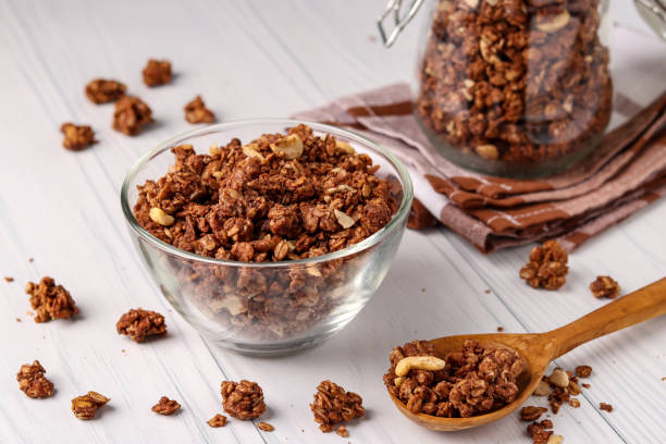 granola knuspriges müsli mit natürlichem honig, schokolade und nüssen in einer glasschüssel vor weißem hintergrund, gesundes essen, horizontale ausrichtung - jar oatmeal granola glass stock-fotos und bilder