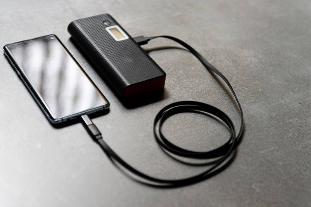 istock Cell phone on desk being loaded. Extra battery concept 1224882593