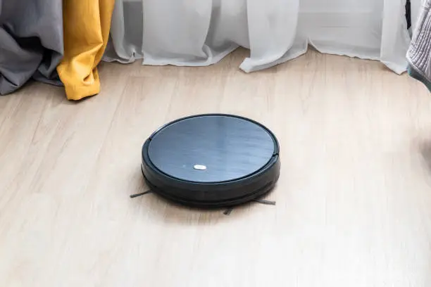 Modern technology concept. Technological cleaning of the room. Black robotic vacuum cleaner cleans the floor in the room