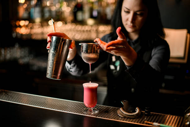 istock brunette woman bartender pours cocktail from shaker into glass using sieve. 1224883878