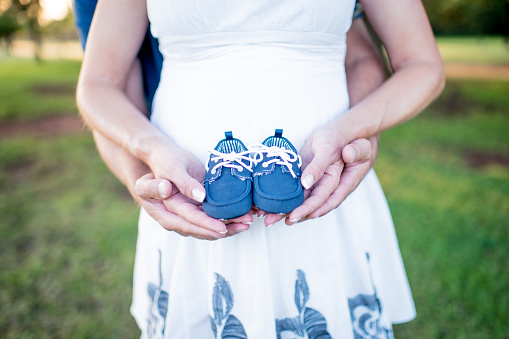 Blue baby shoes of unborn son held by both parents.