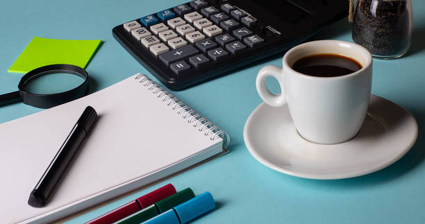 istock Notepad with office supplies and coffie on blue background 1224889511