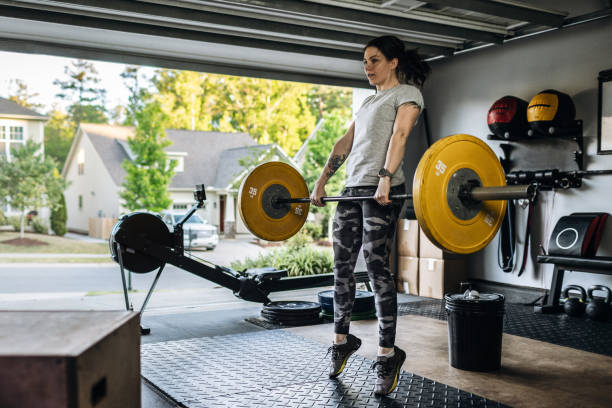 Young woman exercising with heavy barbell in her home garage gym during covid-19 pandemic. - fotografia de stock