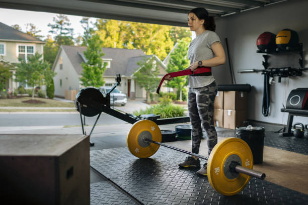 Young woman tightens her weightlifting belt in her home garage gym during covid-19 pandemic. - fotografia de stock
