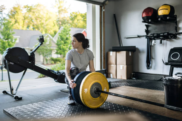 Sporty woman loading weights on the barbell in her home garage gym during covid-19 pandemic. - fotografia de stock