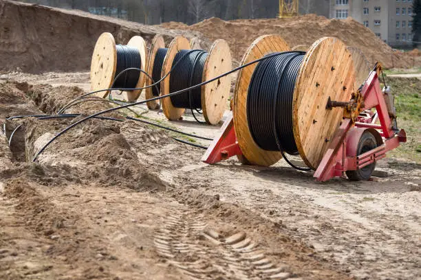 Several wooden coils with power cable laid in a trench. Concept of electricity supply for construction projects.