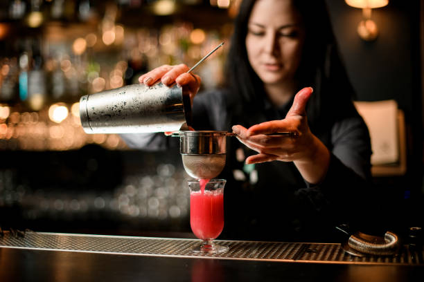 istock woman bartender professionally pours cocktail from shaker into glass using sieve. 1224894443