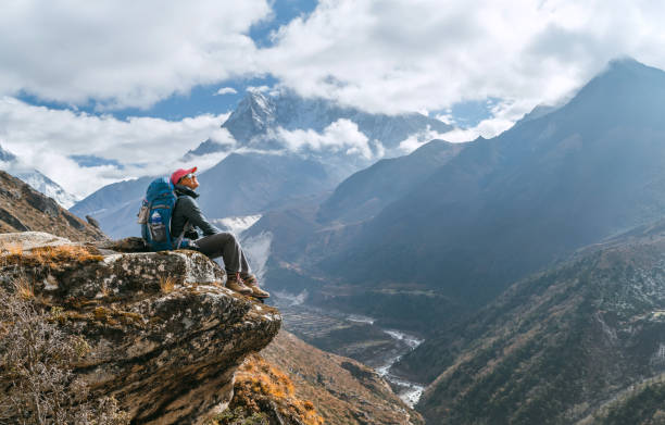 młoda turystka z plecakiem siedząca na krawędzi klifu i ciesząca się szczytem ama dablam 6812 m podczas szlaku trekkingowego everest base camp (ebc) w pobliżu phortse w nepalu. koncepcja obrazu aktywnych urlopów - snow valley mountain mountain peak zdjęcia i obrazy z banku zdjęć