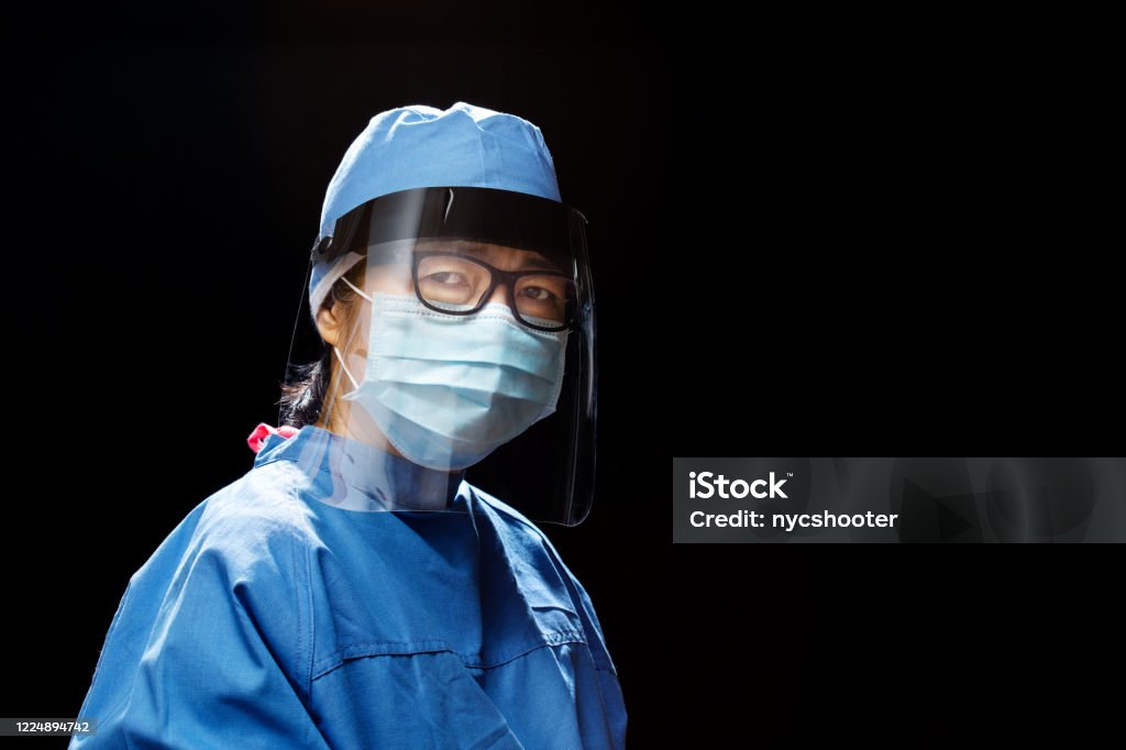 portrait of Healthcare Worker wearing face shield portrait of a Doctor or nurse wearing face shield and mask during the coronavirus pandemic; photographed against black background Nurse Stock Photo