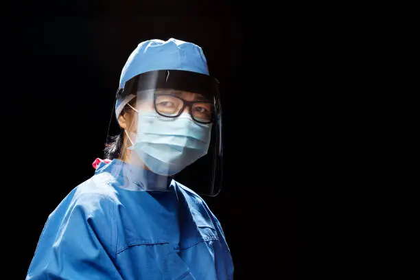 portrait of a Doctor or nurse wearing face shield and mask during the coronavirus pandemic; photographed against black background