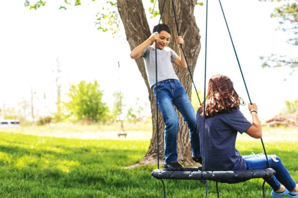 teenage sister and pre adolescent brother swinging on swing in backyard together - freedom tire swing tire swing imagens e fotografias de stock