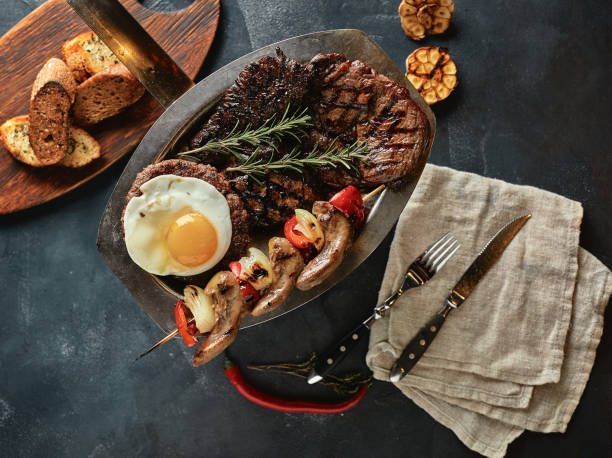 istock Assorted grilled meat, vegetables and spices, a kitchen table for serving meat, with napkins spread out and knives 1224898492