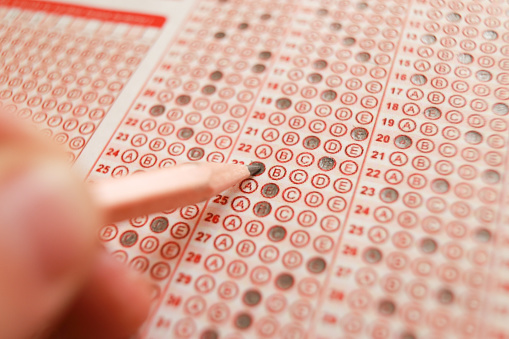 Students hand doing exams quiz test paper with pencil drawing selected choice on answer sheets at school