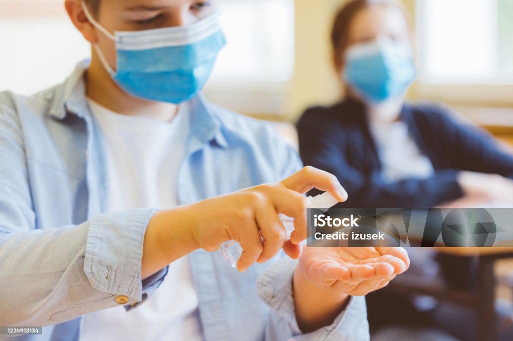 Using hand sanitizer in the classroom School students wearing N95 face masks and using hand sanitizer. Sitting in a classroom. Adolescence Stock Photo