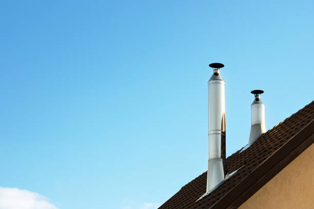 Two modern style chimneys from oven and fireplace stacked stainless steel on tiled roof made according to fire safety requirements, and to avoid condensation when reaching dew point in flue gases. dos chimeneas de estilo moderno de horno y chimenea de acero inoxidable apilado sobre techo de tejas hechas de acuerdo con los requisitos de seguridad contra incendios y para evitar la condensación al llegar al punto de rocío en los gases de combustión.