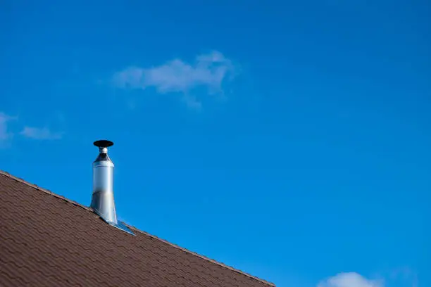 Modern style chimney from oven or fireplace stacked stainless steel on tiled roof made according to fire safety requirements, and to avoid condensation when reaching dew point in flue gases.