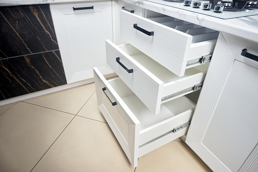 Solution for placing kitchen utensils in modern kitchen - horizontal sliding pullout drawer shelves storage in cupboard for kitchenware cookware under oak countertop gas hob with copyspace.
