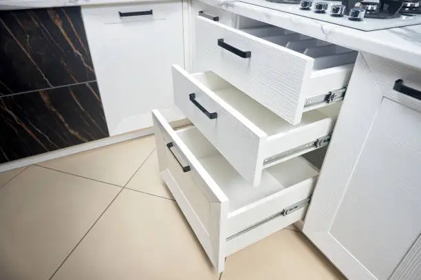Photo of Solution for placing kitchen utensils in modern kitchen - horizontal sliding pullout drawer shelves storage in cupboard for kitchenware cookware under oak countertop gas hob with copyspace.