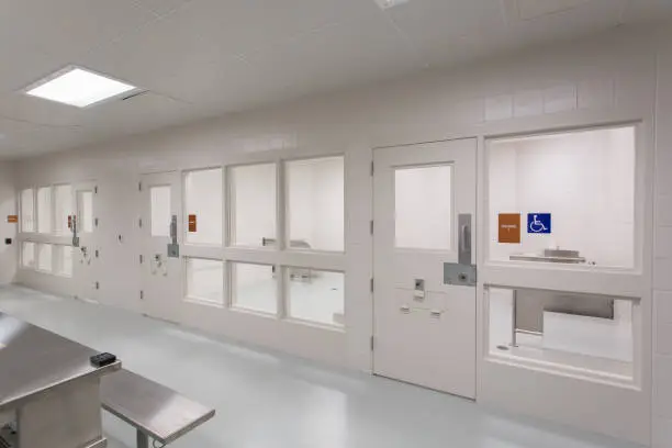 Interior shot of multiple holding cells with glass windows and strong locking doors with pass through hatches. Stainless steel table in open area