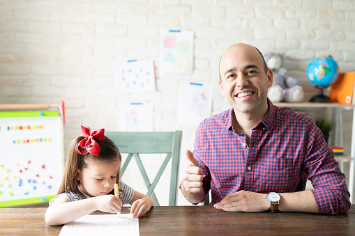 Portrait of a father giving thumbs up and being successful at homeschooling his three year old daughter