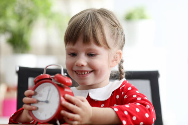 istock Daughter sits at table and holds an alarm clock 1224927511