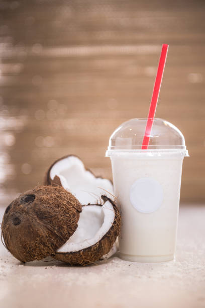 Coconut drink with sliced coconut next to it. With a red straw. Ice cream drink