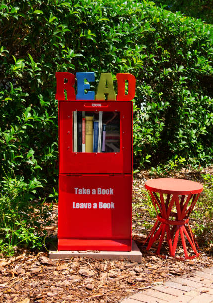 Street library box with sign saying take a book and leave a book with a small bench beside it stock photo