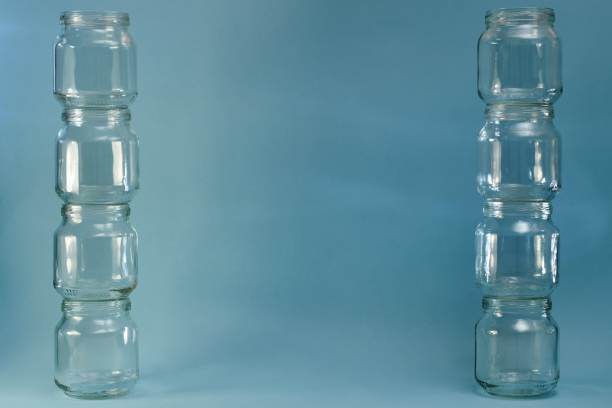 istock Two wide lined vertical parallel rows of glass jars on a blue background. 1224936775