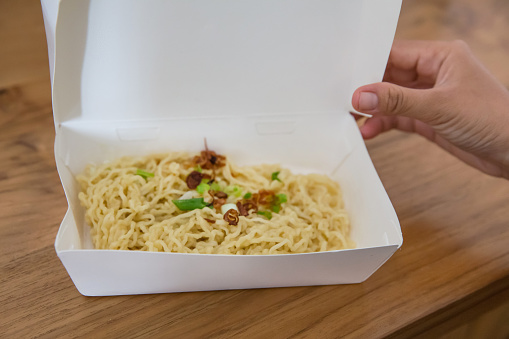 Close up shot of Asian woman opening her takeaway meal box with a vegan stir fry noodles inside, during Coronavirus lockdown