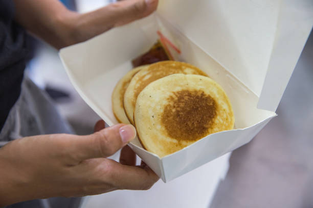 Close up shot of Asian woman opening her takeaway Ramadan Iftar dessert box, with delicious pancakes & savory sauce inside during lockdown Covid 19