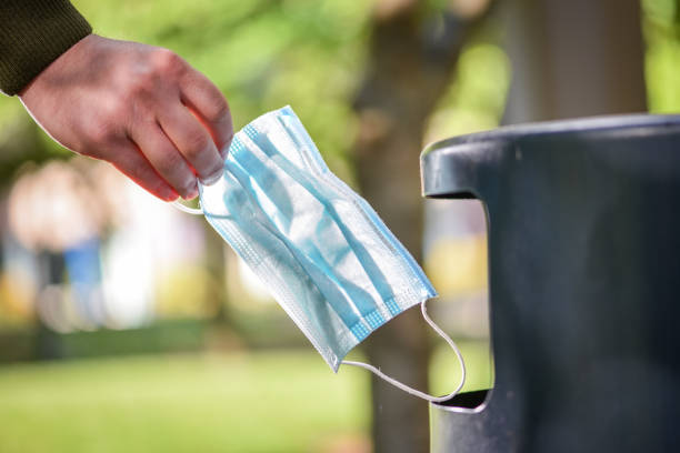 Covid-19 life - positive behavior - Throwing used surgical protective face mask into a garbage bin stock photo