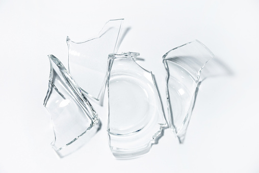Parts of the broken cup jar glass isolated on white background with shadow lighting effect. Pieces of sharp broken glass. Concept of danger.