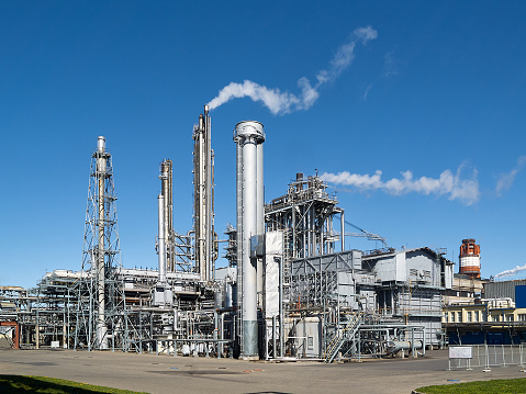 Exterior of a modern silver petrochemical installation with reactors converters furnace chimneys communications over blue sky background with copyspace.