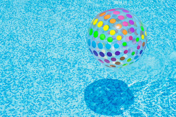 Inflatable colourful ball floating in blue swimming pool water with copy space