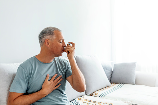 Mature man treating asthma with inhaler at home