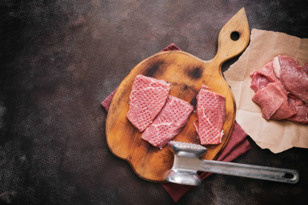 Fresh raw beef meat on a cutting board with a hammer for beating. Top view, flat lay, copy space.