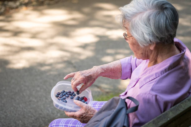 healthy senior asian woman eating fresh blueberries on park bench - 96 well imagens e fotografias de stock