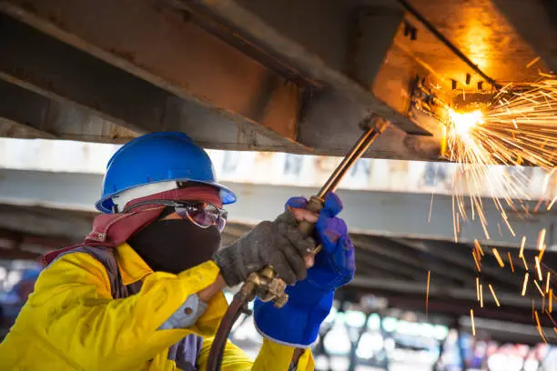 Worker is cutting manually old metal construction in container by using gas mixture of oxygen and acetylene, propane for repair work.