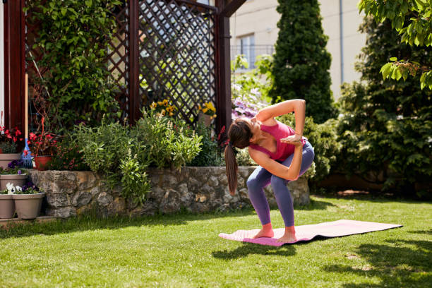 istock Young attractive brunette standing on the mat in her backyard in Revolved Chair position. 1224972903