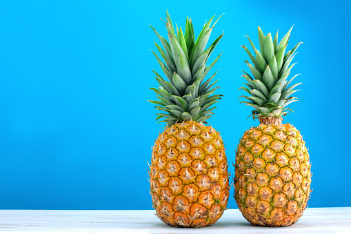 two solid ripe pineapple fruits on white table and blue background
